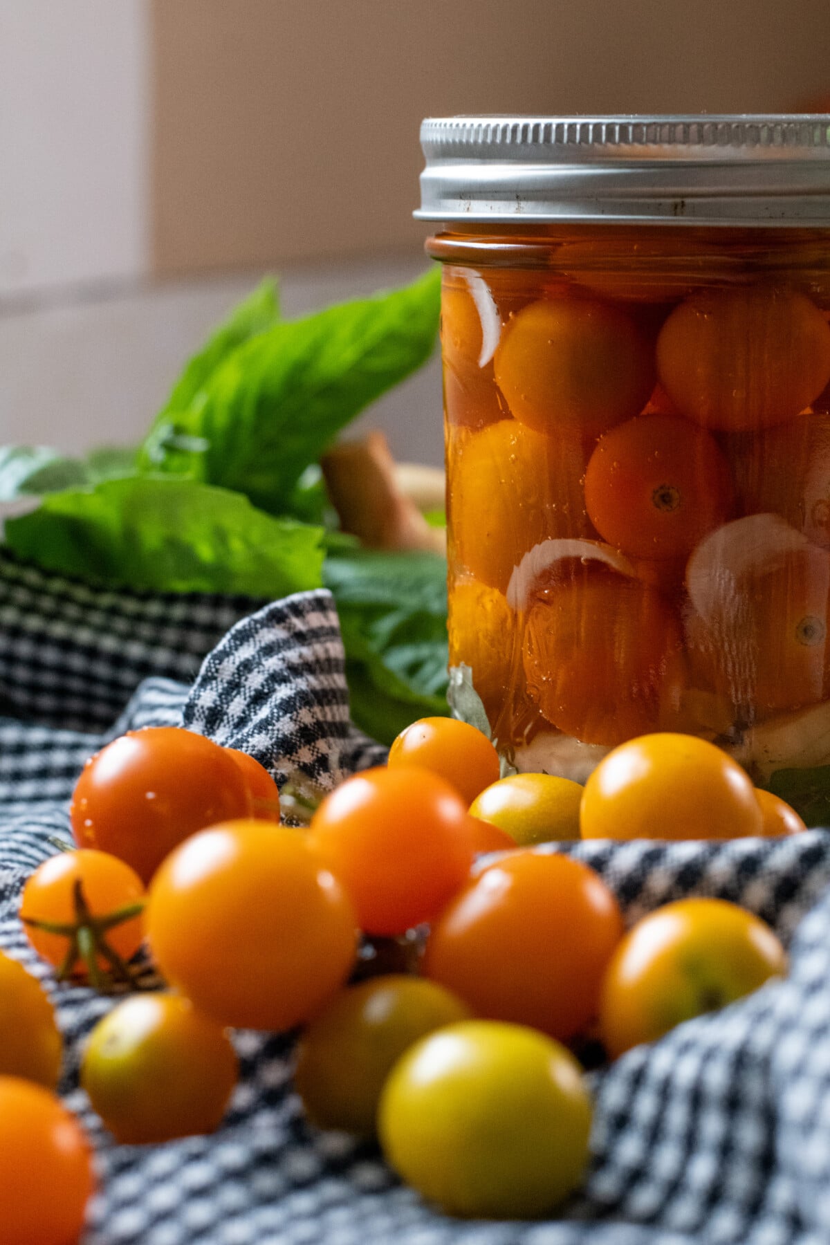 Jar of pickled cherry tomatoes with cherry tomatoes in front of it