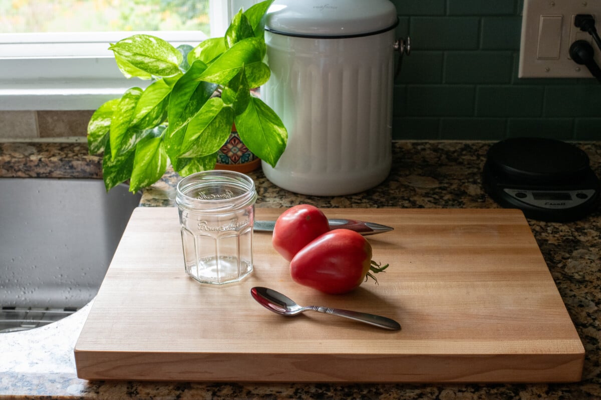 tomatoes, spoon, knife, and jar on a cutting board