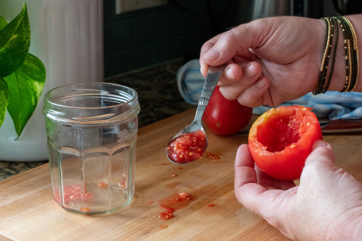 Woman's hands scooping out tomato paste from a tomato