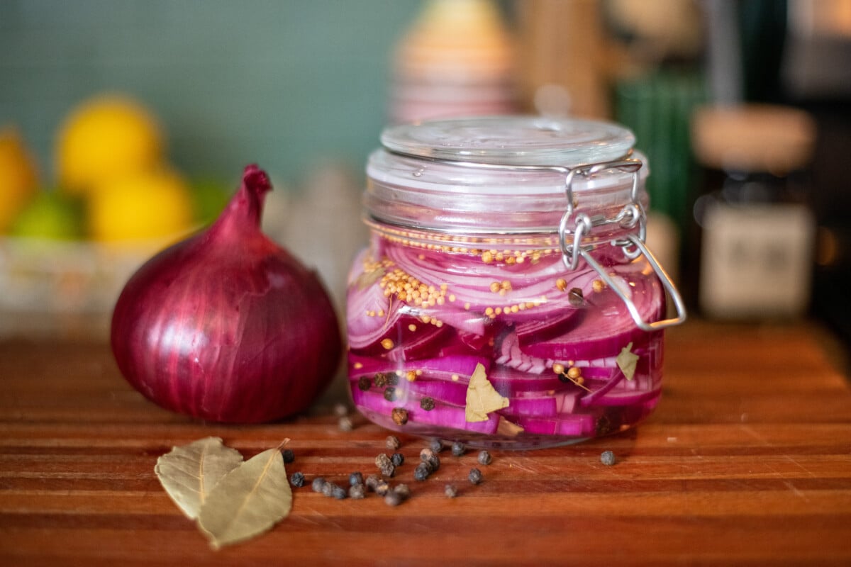 A red onion and a jar of pickled red onions on a cutting board