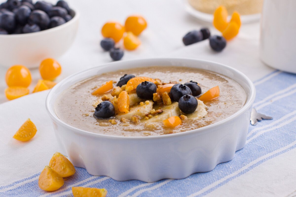A small bowl of amaranth porridge topped with sliced bananas, blueberries and ground cherries.