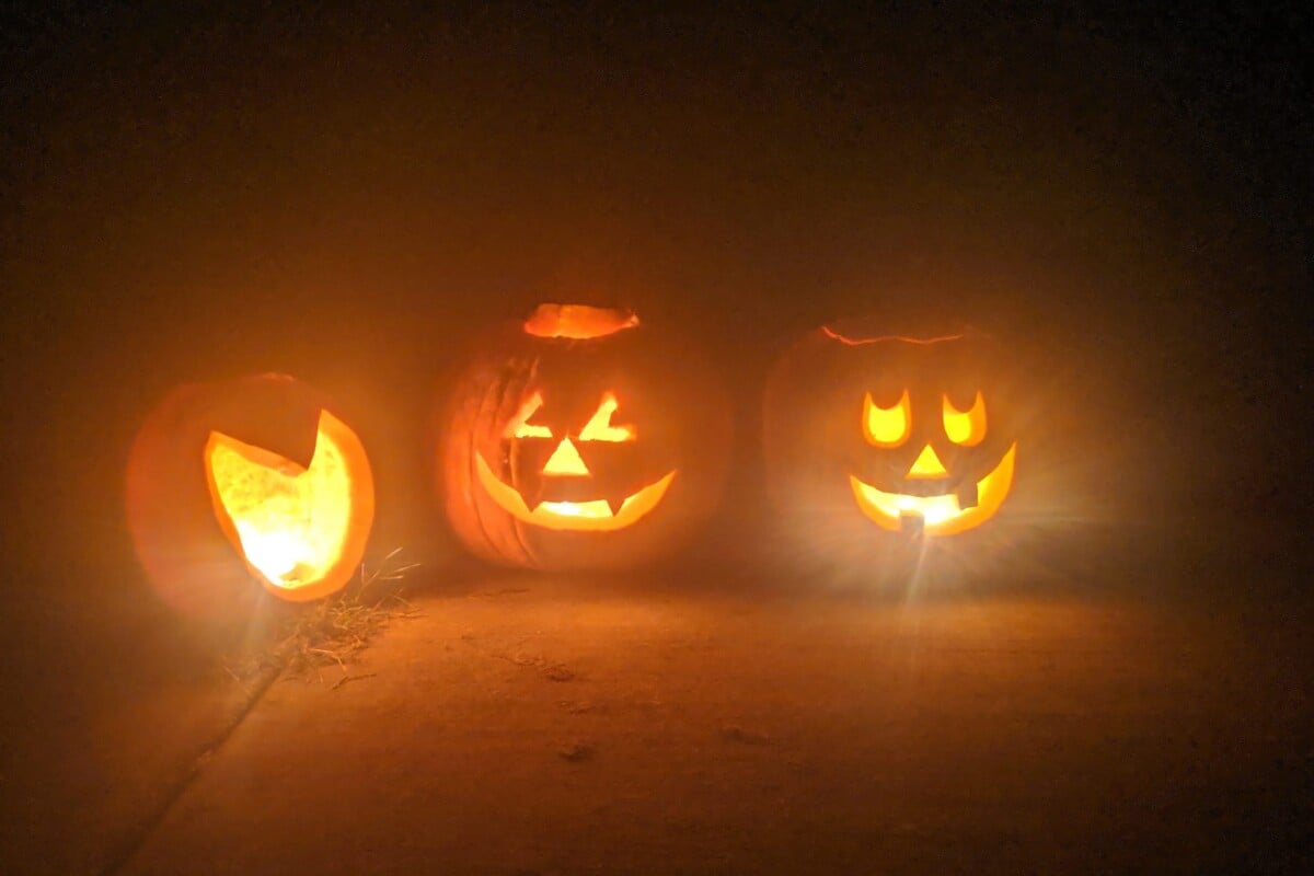 Three brightly lit carved jack-o'-lanterns shining in the dark