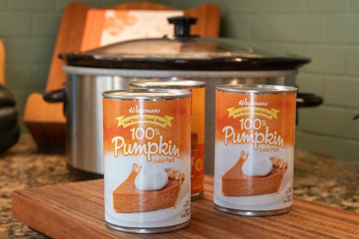 Three cans of solid pack pumpkin in front of a slow cooker