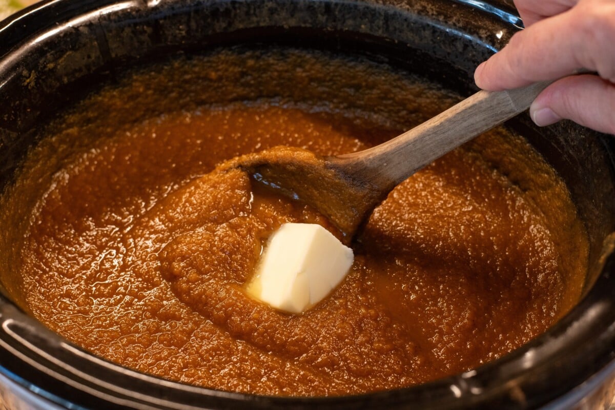 Woman's hand using a wooden spoon to stir in butter into finished pumpkin butter
